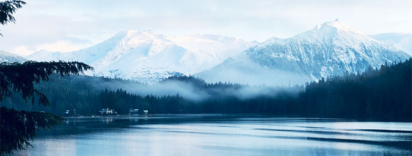 Alaska-Lake-Blue-Water-Mountains-Forest-and-Morning-Fog Blue waters of an Alaskan lake reflecting surrounding trees and distant mountains beneath a layer of mist