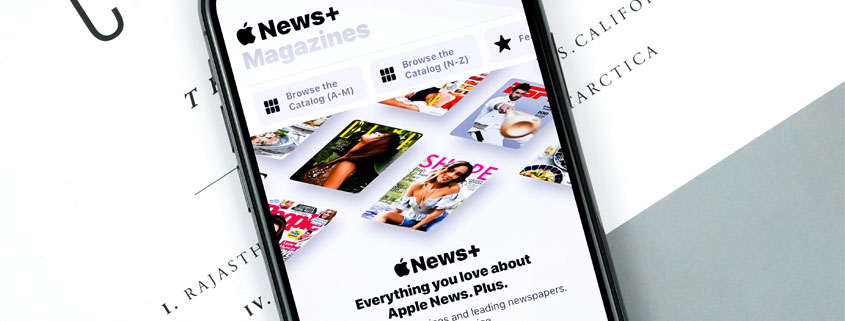 Apple-News-Plus-Digital-News-and-Magazine-Content Smartphone resting on printed papers alongside Apple News Plus promotional text highlighting news and magazine content