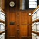 Narrow archive storage aisle in Oxford, UK, lined with shelves of labeled archive boxes, with a locked door and wall clock at the far end