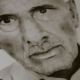Artist's hand carefully drawing details around the neckline of a portrait depicting an elderly bald man