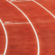 Athlete running along a curved section of a red running track during athletic training