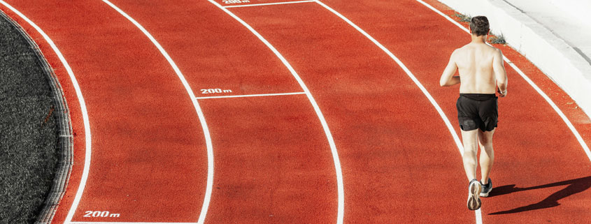 Athlete running along a curved section of a red running track during athletic training