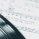 Shiny black vinyl record resting on white sheet music featuring printed musical notes and notation