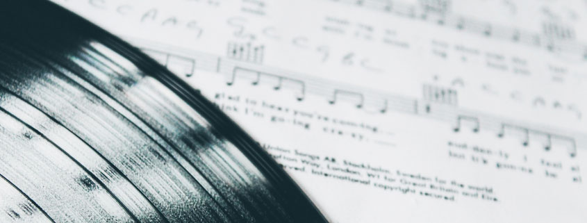 Shiny black vinyl record resting on white sheet music featuring printed musical notes and notation