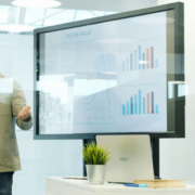 Business professional presenting marketing and sales concepts on a digital whiteboard while colleagues listen during an office meeting