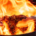 Chef using kitchen tongs to turn meat in a frying pan with controlled flames rising above the food and heat from the stove below