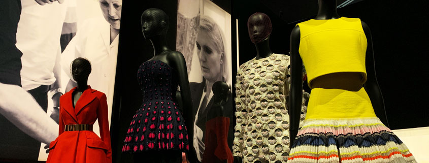 Christian Dior designer dresses displayed on mannequins at the Victoria and Albert Museum in London, featuring elegant red and coordinated haute couture outfits