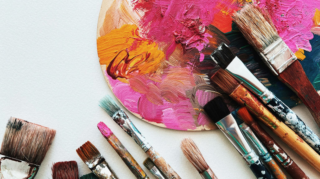 Colorful-Paint-Brushes-and-Artists-Palette Assorted paintbrushes in different sizes surrounded by an artist's palette filled with vibrant paint colors, representing creativity and artistic expression