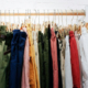Colorful assortment of men's and women's clothing displayed on hangers along a wooden rail mounted against a white wall