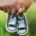 Couple holding hands while each holds a tiny baby shoe, with a wedding ring visible on the woman's hand