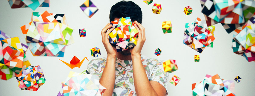 Person holding an intricate geometric paper sculpture made from interconnected folded shapes and cube-like structures
