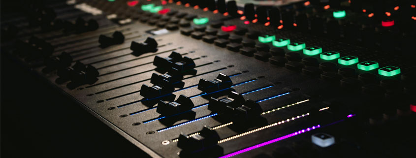 DJ-Mixing-Console-With-Colorful-Illuminated-Controls-at-Party DJ mixing console with brightly illuminated buttons and sound controls in a dark party environment
