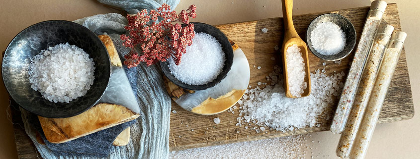 Different-Types-of-Salt-Crystals-and-Coarse-Sea-Salt Assortment of salt crystals in different grain sizes, displayed in small dishes, metal trays, and a wooden scoop