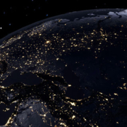 Planet Earth viewed from space at night, with glowing golden city lights illuminating parts of the globe against a dark, star-filled background