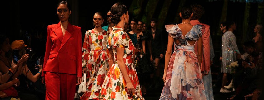 Group of glamorous fashion models walking along a runway in elegant outfits showcasing different clothing designs
