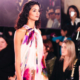 Elegantly dressed woman walking in a long gown while carrying a handbag as spectators watch at a fashion event