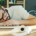 Exhausted man sleeping with his head resting on a closed laptop, surrounded by notebooks, headphones, a phone, and a cup of coffee