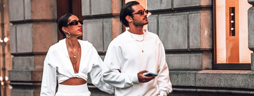 Fashionable-Couple-Wearing-All-White-Outfits-and-Sunglasses Stylish man and woman wearing coordinated all-white fashion outfits and sunglasses, with the man wearing oversized boots