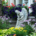 Flower garden featuring an angel statue surrounded by plants near a porch with classical columns