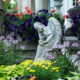 Flower garden featuring an angel statue surrounded by plants near a porch with classical columns