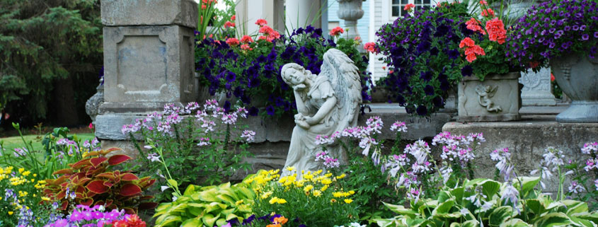 Flower-Garden-With-Angel-Statue-and-Classical-Porch-Columns Flower garden featuring an angel statue surrounded by plants near a porch with classical columns