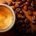 Small cup of freshly brewed espresso topped with crema, surrounded by scattered roasted coffee beans on a wooden table