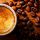 Small cup of freshly brewed espresso topped with crema, surrounded by scattered roasted coffee beans on a wooden table