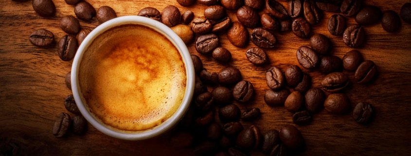 Fresh-Espresso-With-Golden-Crema-and-Roasted-Coffee-Beans Small cup of freshly brewed espresso topped with crema, surrounded by scattered roasted coffee beans on a wooden table