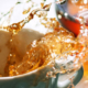 Coffee being poured into a cup from above, with the flowing liquid splashing and spilling over the edges