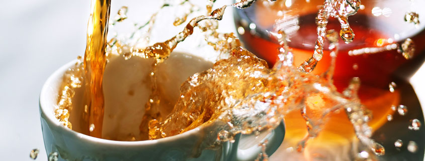 Freshly-Poured-Coffee-Spilling-Over-Cup Coffee being poured into a cup from above, with the flowing liquid splashing and spilling over the edges