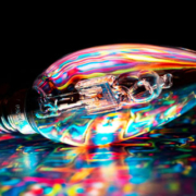 Light bulb glowing with multiple vibrant colors while resting on a colorful surface, symbolizing creative ideas