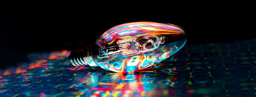 Glowing-Multicolored-Light-Bulb-on-Colorful-Surface Light bulb glowing with multiple vibrant colors while resting on a colorful surface, symbolizing creative ideas