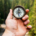 Hand holding a navigation compass toward a distant forest while searching for direction through the natural landscape