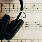 Pair of headphones resting on printed guitar chord diagrams with grids, X and O markings, and finger placement instructions