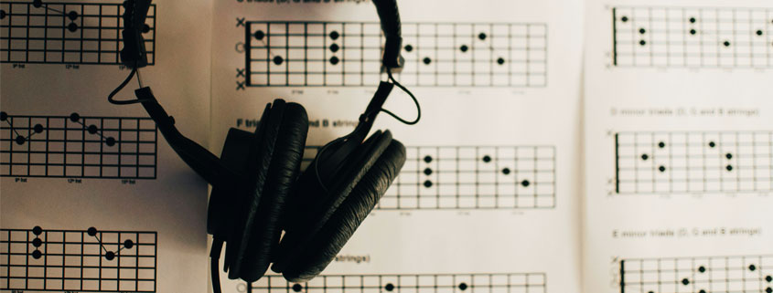 Pair of headphones resting on printed guitar chord diagrams with grids, X and O markings, and finger placement instructions