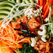Colorful assortment of healthy foods featuring strawberries, avocado, blueberries, mango, carrots, nuts, and sushi arranged on a plate