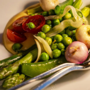 Plate of fresh vegetables including green peas and tomatoes, accompanied by a fork and spoon