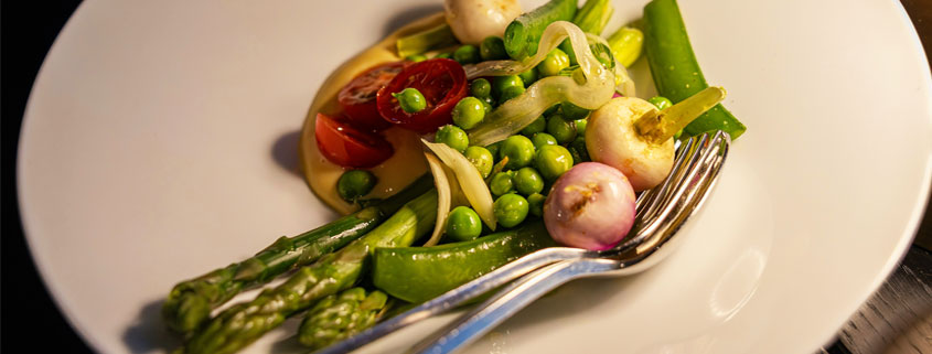 Plate of fresh vegetables including green peas and tomatoes, accompanied by a fork and spoon