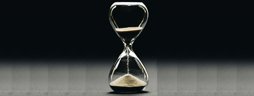 Traditional glass hourglass with sand falling from the upper chamber into the lower chamber, symbolizing the passage of time