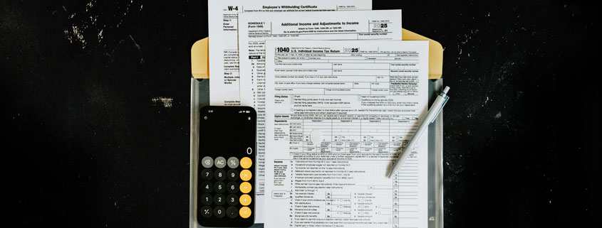 IRS Form 1040 and W-4 tax documents arranged on a clipboard with a calculator and pen
