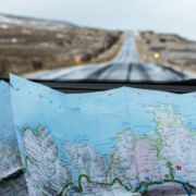 View from inside a car traveling along a road in Iceland, with an unfolded paper map resting on the dashboard for navigation