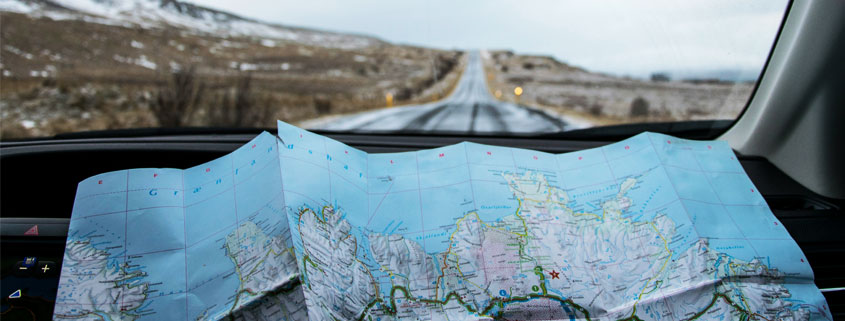 Iceland-Road-Trip-With-Paper-Map-on-Car-Dashboard View from inside a car traveling along a road in Iceland, with an unfolded paper map resting on the dashboard for navigation