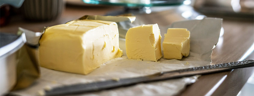 Large-Yellow-Butter-Block-With-Two-Cut-Slices Large block of golden-yellow butter with two neatly cut slices showing its smooth texture and rich color