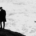 Lone man standing near the edge of a rocky coastal cliff overlooking powerful ocean waves crashing against the rocks below