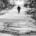 Lone man running uphill along a snow-covered forest trail surrounded by tall trees on both sides