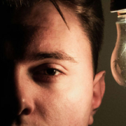 Man looking straight ahead with one side of his face illuminated by a glowing light bulb while the opposite side remains in darkness