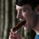 Man with his mouth open, preparing to bite into a sausage