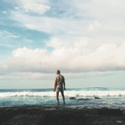 Man standing alone on the shoreline, looking out toward the sea as large waves roll across the water