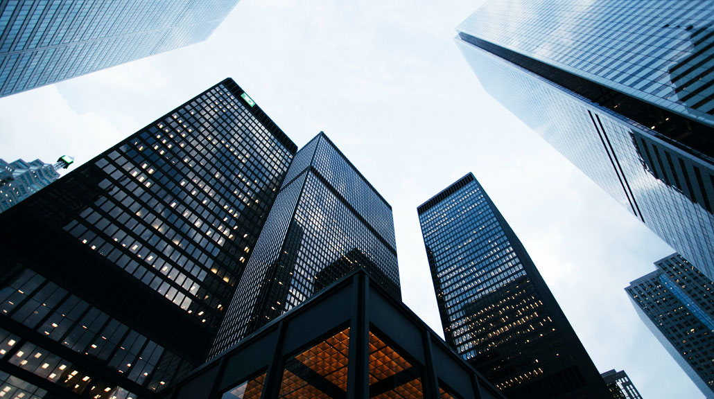 Upward view of modern office skyscrapers surrounding a business district, highlighting corporate architecture and urban development