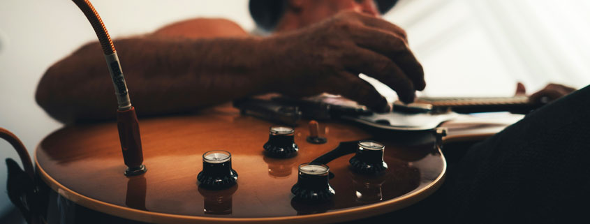 Musician-Playing-Electric-Guitar-Connected-by-Audio-Cable Musician playing an electric guitar connected by an audio cable, appearing focused on the instrument during a creative musical session